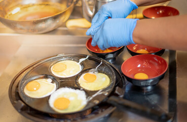 Chef wearing surgical gloves and cooking fried egg prepare made to order with the lunch box for taking home
