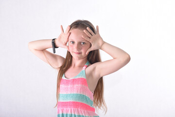 A beautiful school-age girl in the studio on a white background plays scenes with palms and fingers...