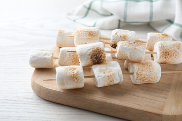 Sticks with roasted marshmallows on white wooden table, closeup
