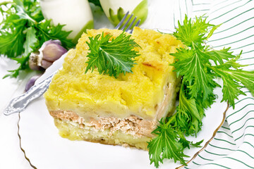 Casserole with potatoes and fish in plate on white wooden board