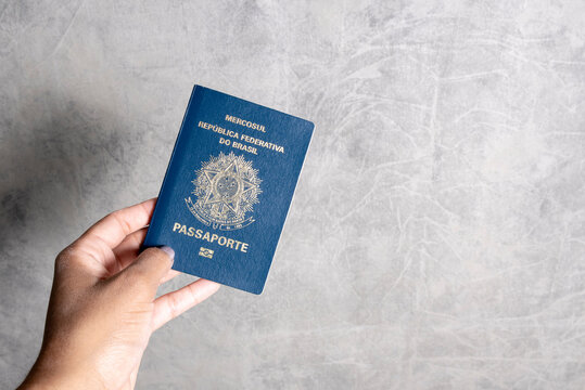 woman holding hand with Brazilian passport on gray background.