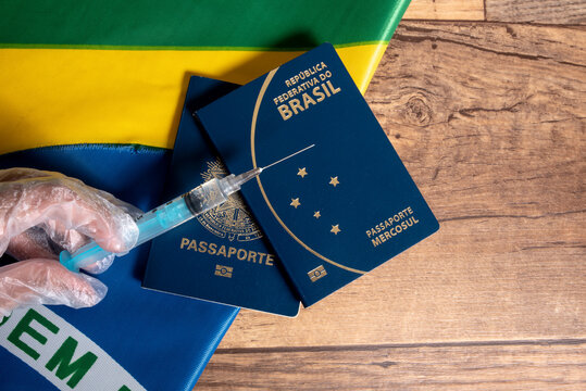 Hand holding COVID-19 vaccine syringe, Brazilian flag, passaport, and wooden background with space for text.