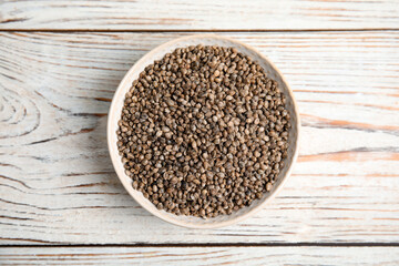 Bowl with organic hemp seeds on white wooden table, top view