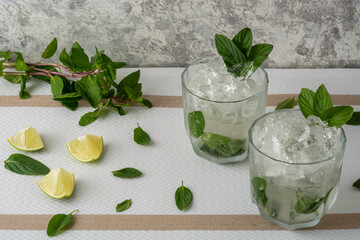 Mojito servido en vaso de cristal con rebanadas de limon y hojas de menta, sobre una mesa de color blanco y fondo vintage