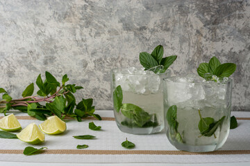 Mojito servido en vaso de cristal con rebanadas de limon y hojas de menta, sobre una mesa de color blanco y fondo vintage