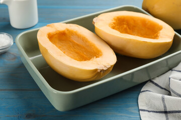 Raw spaghetti squash halves in baking dish on light blue wooden table, closeup