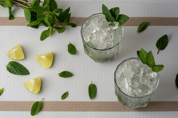Mojito servido en vaso de cristal con rebanadas de limon y hojas de menta, sobre una mesa de color blanco y fondo vintage