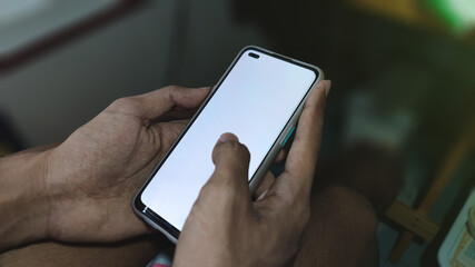 Hand holding Mockup mobile phone with blank white screen in home or coffee shop. A blank phone screen to put content or ads, advertise.