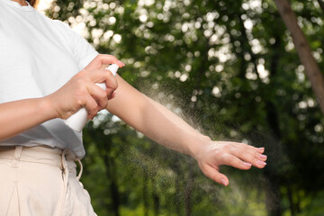 Woman applying insect repellent on arm in park, closeup. Tick bites prevention