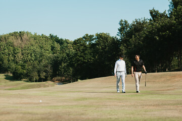 Obraz premium Golfers happily walking with golf clubs on green grass in the morning