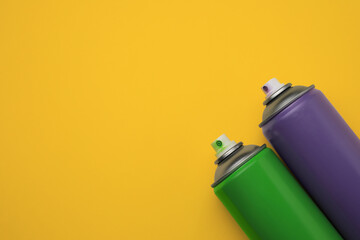 Cans of different graffiti spray paints on yellow background, flat lay. Space for text