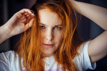 Fototapeta premium Portrait of beautiful adult young woman with red tousled hair, close-up, blurred background. Sexy brunette touches her long hair and looks at camera.