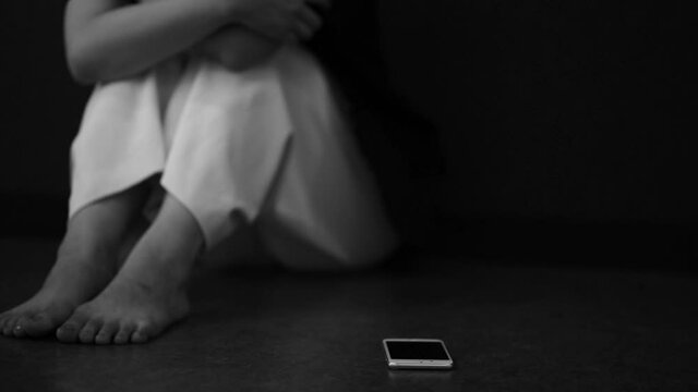 スマートフォンを床に置き落ち込む女性
