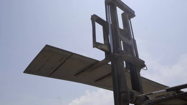 Heavy sheets of steel are held aloft by arms of two huge forklifts