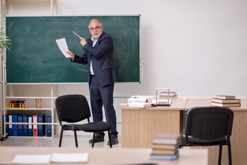 Old male teacher in front of blackboard