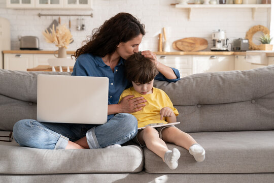 Loving mom kiss small son in head. Remote worker or freelancer woman balancing between career and motherhood embrace little kid using laptop computer to work from home. Mother and child on lockdown
