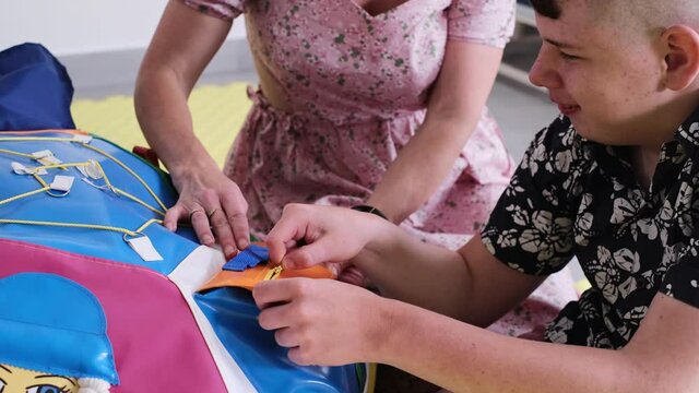 Children with disability getting sensory activity with toys, balls, small objects, cerebral palsy boy playing calming game, training fine motor skills. Rehabilitation center with therapist, mother