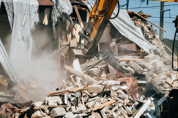 Destruction of old house by excavator. Bucket of excavator breaks concrete structure.