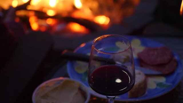 close-up shot of glass of wine and platter near firepit in camping site during winter season