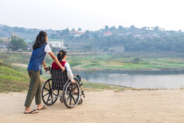 Obraz premium Disabled handicapped woman in wheelchair and care helper walking in park.