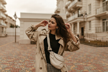Obraz premium Cool young woman in stylish trench coat poses outside. Portrait of attractive lady in good mood looks away.