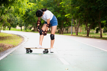 Woman surf skate board putting on elbow protector pads on her arm and wearing wrist guards and...