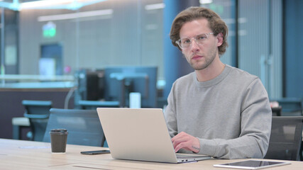 Fototapeta premium Young Man Looking at Camera while using Laptop in Office