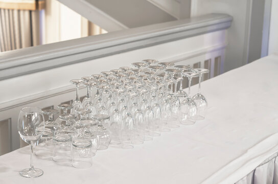 Inverted Glass Goblets And Party Glasses. White Wooden Tabletop Against The Backdrop Of The Kitchen Counter (room)  Use A Key Visual Layout For Product Demo Or Design.