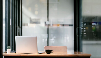 Rear view of laptop computer and  coffee cup on wooden table in modern office room with copy space.