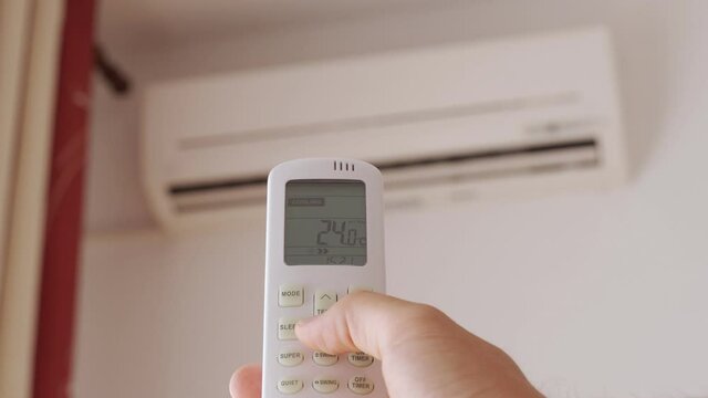 Close-up of man hand is turn-on air conditioner split type by remote controller.