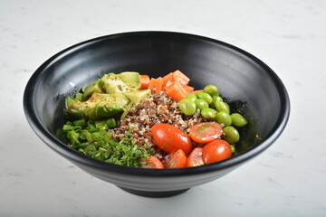 trio quinoa grain salad bowl with avocado, tomato, pea bean, carrot and brown rice in black bowl in white marble healthy poke bowl menu