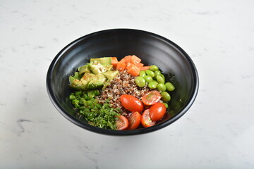 trio quinoa grain salad bowl with avocado, tomato, pea bean, carrot and brown rice in black bowl in white marble healthy poke bowl menu