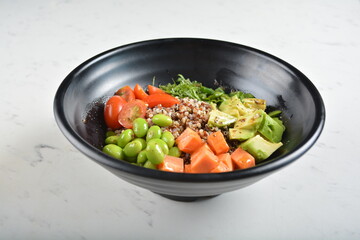 trio quinoa grain salad bowl with avocado, tomato, pea bean, carrot and brown rice in black bowl in white marble healthy poke bowl menu