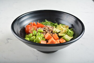 trio quinoa grain salad bowl with avocado, tomato, pea bean, carrot and brown rice in black bowl in white marble healthy poke bowl menu