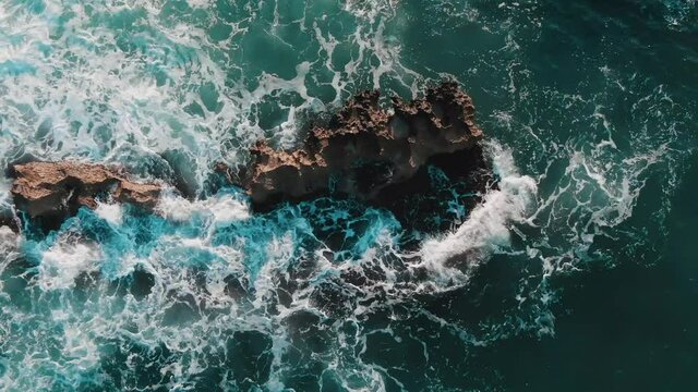 Top Down View Of Foamy Ocean Waves Splashing On Rocks At Capitolo Beach In Puglia Region, Italy - aerial drone shot