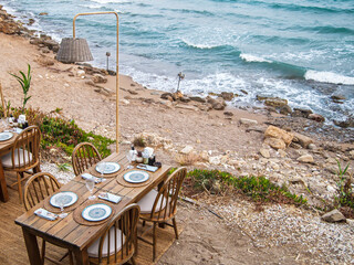 Cafe with wooden tables and chairs at seaside. Turquoise ocean water, blue cloudless sky. Natural background for summer holidays, soft focus, place for text