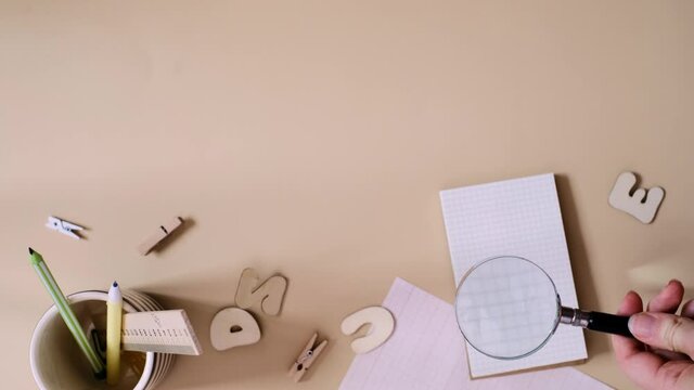 Search idea concept on blank paper, copy space. Person searching with magnifying glass in the notebook with school supplies on the beige background. Flat Lay. Vertical video frame 9x16