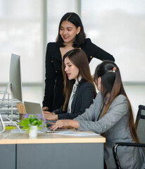 Group of three attractive Asian female office colleagues in formal business suits working together...