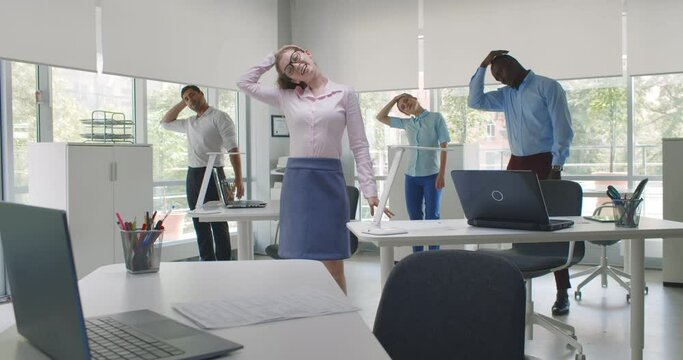 Cheerful diverse colleagues doing neck stretching exercise standing in office