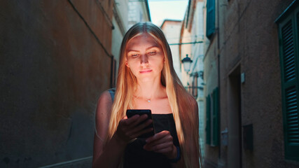 Close-up of blonde woman sharing her impressions from summer trip on video call on smartphone while walking the city of her visit