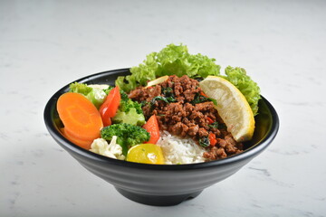 asian spicy thai basil minced pork rice bowl with fried vegetable salad in black bowl in white marble healthy poke bowl menu