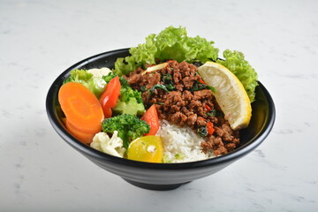 asian spicy thai basil minced pork rice bowl with fried vegetable salad in black bowl in white...