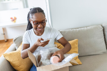 Young satisfied happy african girl woman lady shopaholic customer sit on sofa unpack parcel...