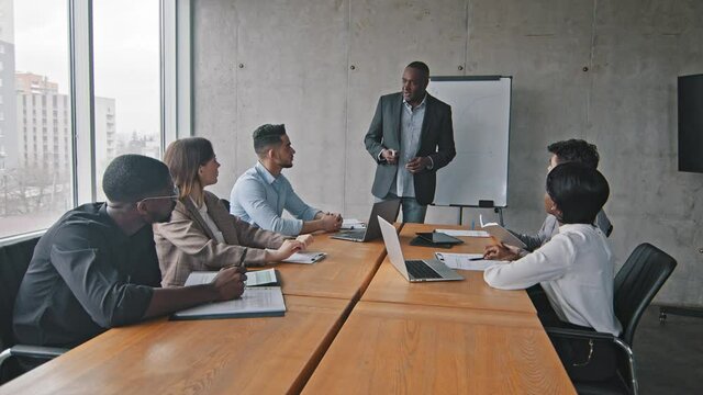Multiracial business team group diverse partner multiethnic colleagues sitting at table in office company at meeting brainstorm listening to lecture presentation of mature African male boss leader