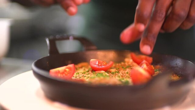 Chef adding ingredients to prepare traditional shakshuka dish, close up view