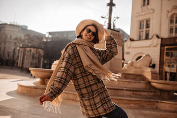 Attractive woman walks around city center. Beautiful lady in checkered coat, hat and sunglasses...