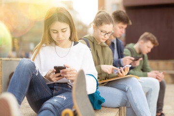 Teenage friends spending time together on streets of city, messaging on their smartphones