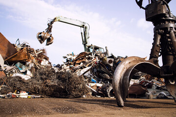 Metal junk yard with hydraulic lifting machine and mechanical grabber for scrap metal recycling.