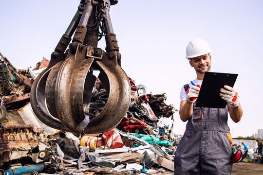 Man controlling process of industrial scrap metal recycling at junk yard.