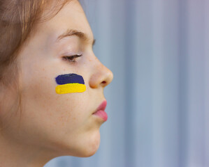 proud face of a Ukrainian girl in profile with a national blue and yellow flag on her cheek. sport and fans support concept. patriotism and independence of Ukraine.
